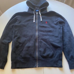 Ralph lauren zip hoodie svart | Storlek M - ‼️Köp innan 16:30 så fraktas tröjan idag‼️Snygg och klassisk hoodie från Ralph Lauren, i svart med dragkedja och det ikoniska röda polo-logotrycket på bröstet. 	•	Storlek: M 	•	Färg: Svart 	•	Modellen har två fickor framtill. Skicket är fint, normal användning men inga större fel, säljer tröjan för den inte används längre😀