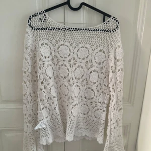 Vit spetsblus med blommigt mönster - Superfin vit blus i spets med blommigt mönster och långärmade ärmar. Blusen har en vid och luftig passform, rundad hals och detaljerade virkade kanter. Perfekt för dig som gillar boho-vibe och vill sticka ut med en unik topp.