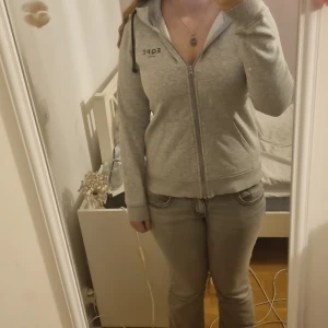 Grå hoodie från EQPE med dragkedja - Säljer en grå hoodie från EQPE i storlek S. Tröjan har huva med snörning, hel dragkedja framtill och två fickor. Mjuk insida i fleece och stilren design med EQPE-logga på bröstet. Perfekt för chill dagar eller när du vill vara extra comfy.