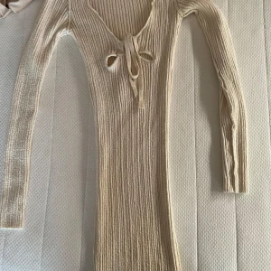 Beige ribbad strandklänning från bershka - Säljer en beige ribbad klänning med snygg v-ringning och snörning framtill. Klänningen har långa ärmar, är figurnära i modellen och mycket stretchig. Superfin till stranden eller semestern🌴