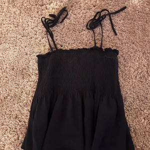 Marinblått linnetopp med knytband - Snygg marinblått linnetopp med smockad överdel och tunna axelband som knyts upptill. Toppen har en luftig och flowy passform nedtill, perfekt för varma dagar. Enkel att matcha med både jeans och kjol.