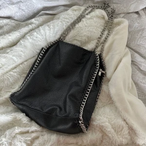 Tiamo axelväska - Axelväska från Tiamo i skinnimitation med silverkedjor. I perfekt skick och varsamt använd. ❤️ Likt Stella Mccartney, köpt på Scorett. Har flera rymliga fickor och är perfekt till skolan eller vardagligt bruk! 