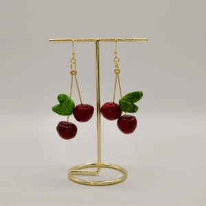 Örhängen med körsbär och blad handgjord 925 silver - Superfina örhängen med hängande körsbär i röd färg och gröna blad, fästa på tunna guldfärgade krokar. Perfekt för dig som vill sticka ut med ett lekfullt och färgglatt smycke. Körsbären har en glansig finish och detaljerade blad som ger extra charm.  Handgjorda örhänge i polymerlera Nickelfria och med silverkrokar guldpläterad stämplade med S925  Totallängd 7,5cm  Bredd 3,5cm  Designad och gjord av Jeanetique