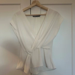 Vit topp ifrån Zara - En super fin topp ifrån Zara med knytdetalj framtill, en liten dragkedja på högra sidan (syns ej när man har den på sig)! Väldigt fint skick!! 