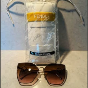 Fendi solglasögon brun - Snygga solglasögon från Fendi med fyrkantiga linser i brun toning och tunn guldfärgad metallbåge. Sidorna har Fendi-logga i metall och glasögonen kommer med originalfodral