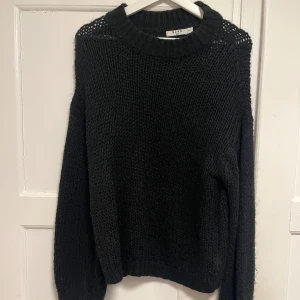 Svart stickad tröja från NA-KD - Säljer en svart stickad tröja från NA-KD med grovstickad struktur och rund hals. Tröjan har långa ärmar och ribbade muddar vid hals, ärmslut och nederkant. Perfekt för att hålla sig varm under kyliga dagar och passar till jeans eller kjol.