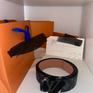  svart monogram bälte - Snyggt svart bälte i skinn med klassiskt monogrammönster i grått och  som spänne. Insidan är ljusbrun och bältet har exklusiva detaljer. Perfekt accessoar för att lyfta din outfit.