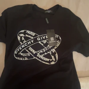 Svart Givenchy t-shirt - Svart t-shirt från Givenchy med vit grafisk print på bröstet där det står 'Givenchy Paris' i ett snirkligt mönster. Klassisk rund hals och korta ärmar. Perfekt för dig som gillar exklusiva märken och stilren design. Kommer utan tagg!!