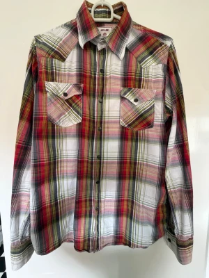 Rutig skjorta från Jack & Jones - Säljer en långärmad rutig skjorta från Jack & Jones i rött, vitt, svart och gult. Skjortan har två bröstfickor med lock och knappar framtill. Perfekt för dig som gillar en klassisk men färgstark stil.