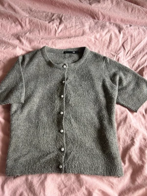 Stickad kofta  - Grå kortärmad stickad  kofta med vita glansiga knappar. Original pris (150kr) är i xs men passar även för S 