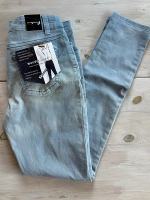 Ljusblå skinny jeans Wonderjeans - Snygga ljusblå skinny jeans med klassisk femficksdesign och hög midja. Jeansen har en stretchig passform som sitter tajt längs benen och är perfekta för en trendig look. Materialet är mjukt och bekvämt, vilket gör dem lätta att bära hela dagen. Helt nya!