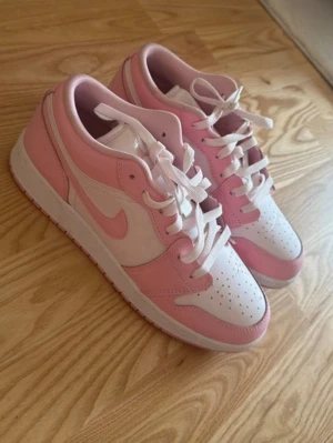 Rosa och vita låga sneakers - Snygga sneakers i vitt och ljusrosa med klassisk siluett och perforerad tåbox. Skorna har vita snören och rosa detaljer längs sidorna och runt hälen. Tillverkade i slätt lädermaterial och har en låg profil som passar till många olika stilar.