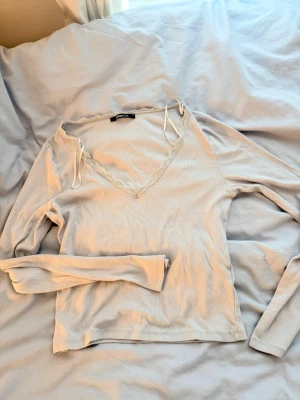 Ljusblå långärmad topp med spets - Supersöt ljusblå ribbad topp från Gina Tricot med lång ärm och v-ringning. Spetsdetaljer och tunna band vid halsen ger en romantisk vibe. Perfekt att styla med jeans eller kjol för en trendig look. Oanvänd!!!!