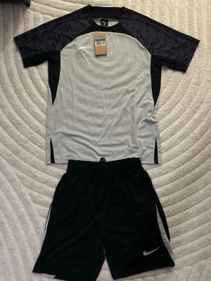 Nike svart och grått träningsset - Grå och svart träningsset från Nike. Storlek M helt ny och Oanvänd. Perfekt för sommarn, fotboll, gym eller löpning. Fraktas inom 24 timmar efter köp📦🚛