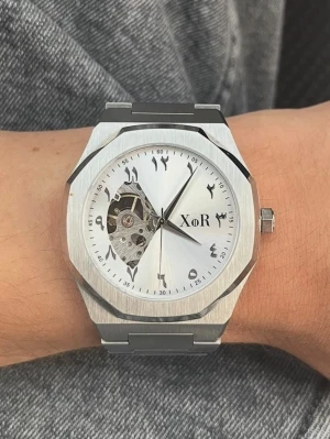 Silverfärgad automatisk klocka XoR - Stilren automatisk klocka från XoR i stainless steel och boett. Urtavlan är vit med arabiska siffror och har ett öppet hjärta som visar urverket. Passar perfekt för dig som gillar unika detaljer och modern design. HELT NY!