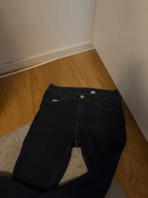 Mörkblå skinny jeans - Säljer ett par mörkblå skinny jeans med klassisk femficksdesign och gulbruna sömmar. Jeansen har hög midja och stängs med knapp och dragkedja. Perfekta till en avslappnad stil och passar till det mesta i garderoben.