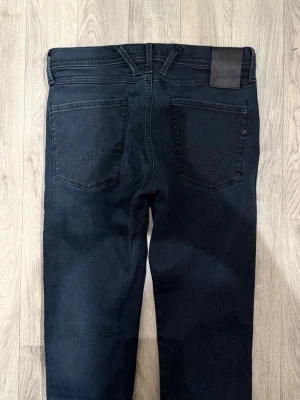 Replay Anbass Hyperflex Jeans Mörkblå W31/L32 - Slim Fit - Replay Anbass Hyperflex mörkblå jeans i stretchig Hyperflex denim med slim fit passform som sitter snyggt och bekvämt och funkar till allt, storlek W31/L32, midja 39 cm, ytterbenslängd 102 cm, benöppning 15 cm, modellen är 185cm & väger 65kg, i fint skick.
