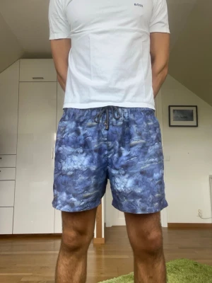 Blå mönstrade badbyxor - Blå mönstrade badbyxor från L’Homme Rouge. Strl M. Inga defekter. Modellen är 178 cm och väger 77 kg. Hör gärna av dig vid frågor!