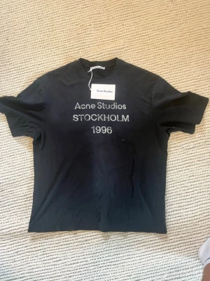 Svart Acne Studios t-shirt - Svart t-shirt från Acne Studios med tryck 'Acne Studios STOCKHOLM 1996' på bröstet. Denna är Storlek L. Helt ny som ni ser med prislappen