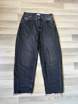 Svarta baggy jeans - Säljer ett par svarta jeans med rak passform och råa, fransiga benslut. Jeansen har klassisk femficksdesign och hög midja. Perfekta för en avslappnad och trendig look.
