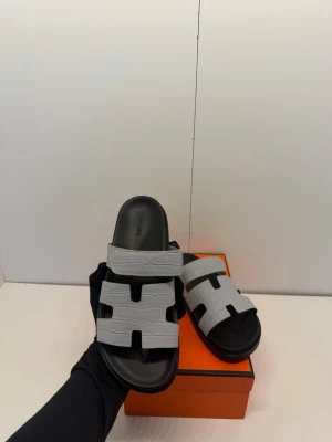 Herméss tofflor - Modellen har den justerbara kardborreremmen upptill som gör att de sitter otroligt bekvämt på foten. En modern "techno-sandal" som lyfter vilken outfit som helst! Detaljer: * Modell: Chypre sandal (unisex) * Färg: Grå / Svart  * Skick: Helt nya i kartong * Storlek: 43 (passar 42/43)  * Medföljer: Originalkartong (orange box) och dustbags Skickas spårbart och säkert emballerat. Hör av dig vid frågor eller om du vill ha fler bilder! ⚡️