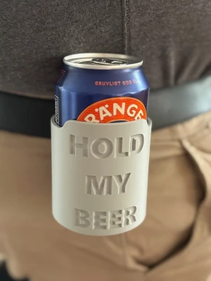 Grå bälthållare för burk - 2 för 80 Praktisk grå bälthållare i plast med texten 'HOLD MY BEER'. Perfekt för att ha en burk nära till hands när du är på språng. Passar de flesta standardburkar och fästs enkelt på bältet.