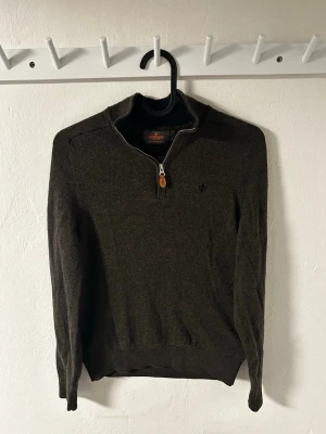 Mörkbrun stickad tröja med halvzip - Mysig mörkbrun stickad tröja med halv dragkedja och ståkrage. Tröjan har långa ärmar, ribbade muddar och en liten broderad logga på bröstet. Perfekt för lager på lager och enkel att matcha till olika outfits. Är size S men sitter mindre som en xs.