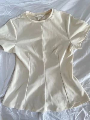 Figursydd vit topp med kort ärm - Säljer fin ljusgul topp. Som ser elegant ut fast passar även bra i vardagen. Den är insyd i sidorna och ger en fin smal silhuett. Original pris. 270kr. Inga söndriga sömmar eller några hål. Är i nytt skick använd ett par gngr. 😊