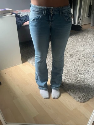Ljusblå bootcut jeans - Säljer ett par ljusblå bootcut jeans med klassisk fyrficksdesign och normal midja. Jeansen har en lätt tvättad look och stängs med dragkedja och knapp. Perfekta för en avslappnad och trendig stil.