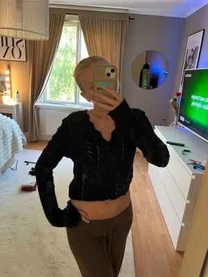 Svart croppad stickad tröja - Svart croppad stickad tröja med v-ringning och långa ärmar. Tröjan har ett genombrutet mönster som ger en cool och trendig look. Perfekt för att styla med höga byxor eller kjol.
