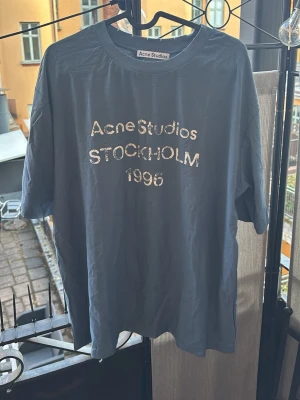 Blå Acne Studios - Snygg blå t-shirt från Acne Studios med vitt tryck på bröstet där det står 'Acne Studios STOCKHOLM 1996'. Klassisk rund hals och avslappnad passform. Perfekt för dig som gillar stilrena plagg med en twist.