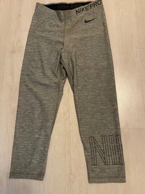 Grå Nike Pro leggings - Snygga gråmelerade Nike Pro leggings med svart logga och bred resår i midjan där det står 'NIKE PRO'. Tillverkade i stretchigt material som sitter tight och bekvämt. Perfekta för träning eller chill. Storlek M men uppskattas som XS/S