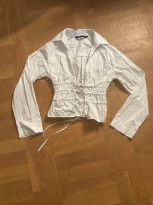 Blus med krage och markerad midja🌟 - Trendig vit croppad blus med långa ärmar och markerad midja med snörning framtill. Blusen har en bred krage och är tillverkad i ett lätt, vävt material som ger en avslappnad men snygg look.