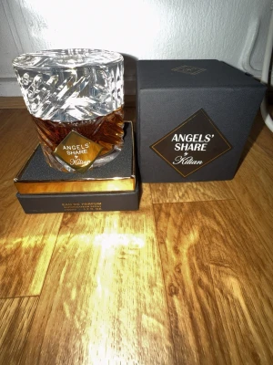 Angels' Share parfym från Kilian - Lyxig parfym från Kilian, Angels' Share, i en elegant glasflaska med kristalliknande lock och bärnstensfärgad vätska. Kommer i exklusiv svart förpackning med gulddetaljer. Perfekt för dig som gillar unika och sofistikerade dofter.