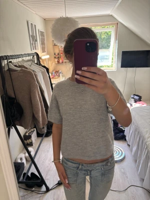 Grå stickad tröja Gina Tricot - Mysig grå stickad tröja från Gina Tricot med korta ärmar och rund halsringning. Tröjan har en enkel och stilren design i mjukt material, perfekt att matcha med jeans eller kjol för en avslappnad look.