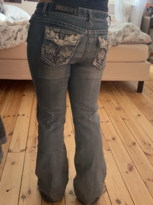 Blå bootcut jeans med broderade fickor - Säljer ett par blå bootcut jeans med snygga broderade bakfickor och detaljerade sömmar. Jeansen har låg midja och en klassisk femficksmodell. Perfekta för dig som gillar en avslappnad men ändå trendig stil. Skulle säga att storleken är M