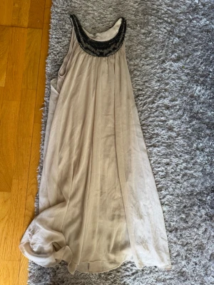 Beige långklänning från DAY - Elegant beige långklänning från DAY Birger et Mikkelsen med dekorativ svart detalj runt halsringningen. Klänningen har en lös passform och är ärmlös, perfekt för sommarens alla tillfällen. Skriv privat för fler bilder eller om du har några frågor💗