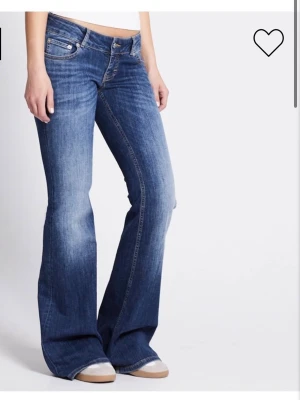 Blå bootcut jeans med låg midja - Säljer ett par klassiska blå bootcut jeans med låg midja och fem fickor. Jeansen har en snygg tvätt och utsvängda ben, perfekta till sneakers eller boots. Tillverkade i denim med en skön passform och coola detaljer vid fickorna. Kort längd.