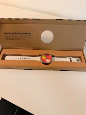 Färgglad klocka med extra armband - Säljer en stilren klocka med vitt silikonarmband och färgglad urtavla i rött, gult och orange. Medföljer även ett extra rött silikonarmband. Perfekt accessoar för dig som gillar att sticka ut med din stil. Project watched breakfast sällsynt designer klocka