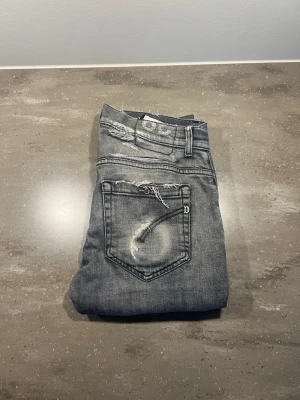 Grå Dondup George  - Tja! Säljer ett par gråa dondup jeans med slitningar och distressed detaljer på fickor och ben. Jeansen har ett hål vi backfickan i en av ringarna samt ett hål på framsidan, men det syns knappt vid användning. Det finns även en liten fläck på baksidan (se bild) men den bör gå bort i tvätten utan problem. Hör av er vid frågor eller funderingar!