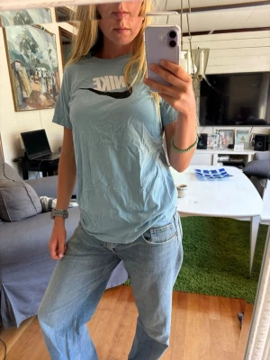 Ljusblå Nike t-shirt med logga - Säljer en ljusblå t-shirt från Nike med stor vit logga och svart swoosh på bröstet. Klassisk passform och rund halsringning. Perfekt till jeans eller shorts för en avslappnad look.