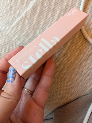 Rebecca Stella Lip Drip Berry Rizz - Rebecca Stella Lip Drip i färgen Berry Rizz. Läppglanset kommer i en snygg rosa förpackning och ger en bärig, djup nyans till läpparna. Perfekt för dig som vill ha glansiga och fylliga läppar med en hint av färg. Modern design och enkel att ta med i väskan.
