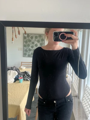 Svart långärmad body - Säljer en stilren svart body med långa ärmar och rund halsringning. Bodyn har en tight passform och är tillverkad i ett mjukt, stretchigt material som sitter snyggt på kroppen. Perfekt att matcha med jeans eller kjol för en clean look.