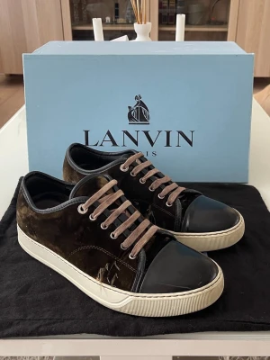 Lanvin Bruna - Säljer ett par bruna Lanvin sneakers i sammet med lackade tåpartier och beigea snören. Skorna har vit sula och klassisk låg profil. Nypris är runt 5000kr                                              Box och påse för skorna kommer med!!. Perfekta för dig som gillar exklusiv och stilren design med en twist av lyxiga material. OBS skorna är lite slitet på sidorna av skorna som man kan se på bilderna.