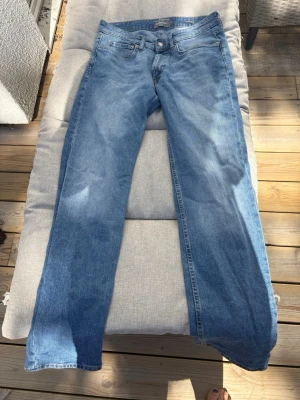 Blå raka jeans från Dressmann - Klassiska blå jeans från Dressmann med rak passform och fem fickor. Jeansen har normal midja och är tillverkade i slitstarkt denimtyg med snygga kontrastsömmar. Perfekta för en avslappnad och stilren look.