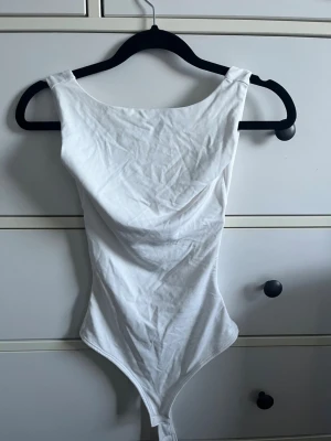 Vit basic body med breda axelband - Säljer en enkel och stilren vit body med breda axelband och rundad halsringning. Bodyn har en klassisk, tight passform och är tillverkad i mjukt stretchigt material, perfekt att matcha med jeans eller kjol. Den saknar lappar men är aldrig använd utan endast provad! 
