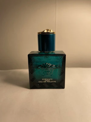 Versace Eros Eau de Toilette 30ml - Ca 50 % kvar. Versace Eros Eau de Toilette i en elegant turkos glasflaska med guldiga detaljer och Medusa-huvud på framsidan. Flaskan har en fyrkantig form och lock i matchande färg med guldkant. En ikonisk doft som sticker ut i badrumshyllan. 
