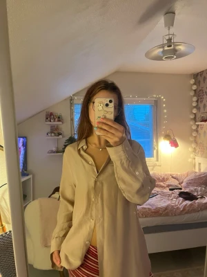  Filippa K Oversized beige skjorta - Säljer en oversized beige skjorta med klassisk krage och knäppning framtill. Skjortan har långa ärmar med manschett och är tillverkad i ett mjukt, flowy material som ger en avslappnad look. Perfekt att styla lager på lager eller bära som den är. 100% silk. 