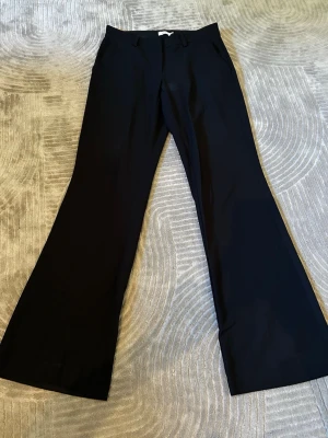 Svarta utsvängda kostymbyxor - Snygga svarta kostymbyxor med low midja och utsvängda ben. Klassisk design med hällor för skärp och sidfickor. 