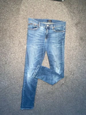 Polo Ralph lauren jeans - Snygga blå slim fit jeans med lätt slitna detaljer och klassisk femficksdesign. Jeansen har normalhög midja och smala ben. Tillverkade i denim med stretch för extra komfort. Perfekta för en avslappnad och trendig look. Har defekt vid höften.